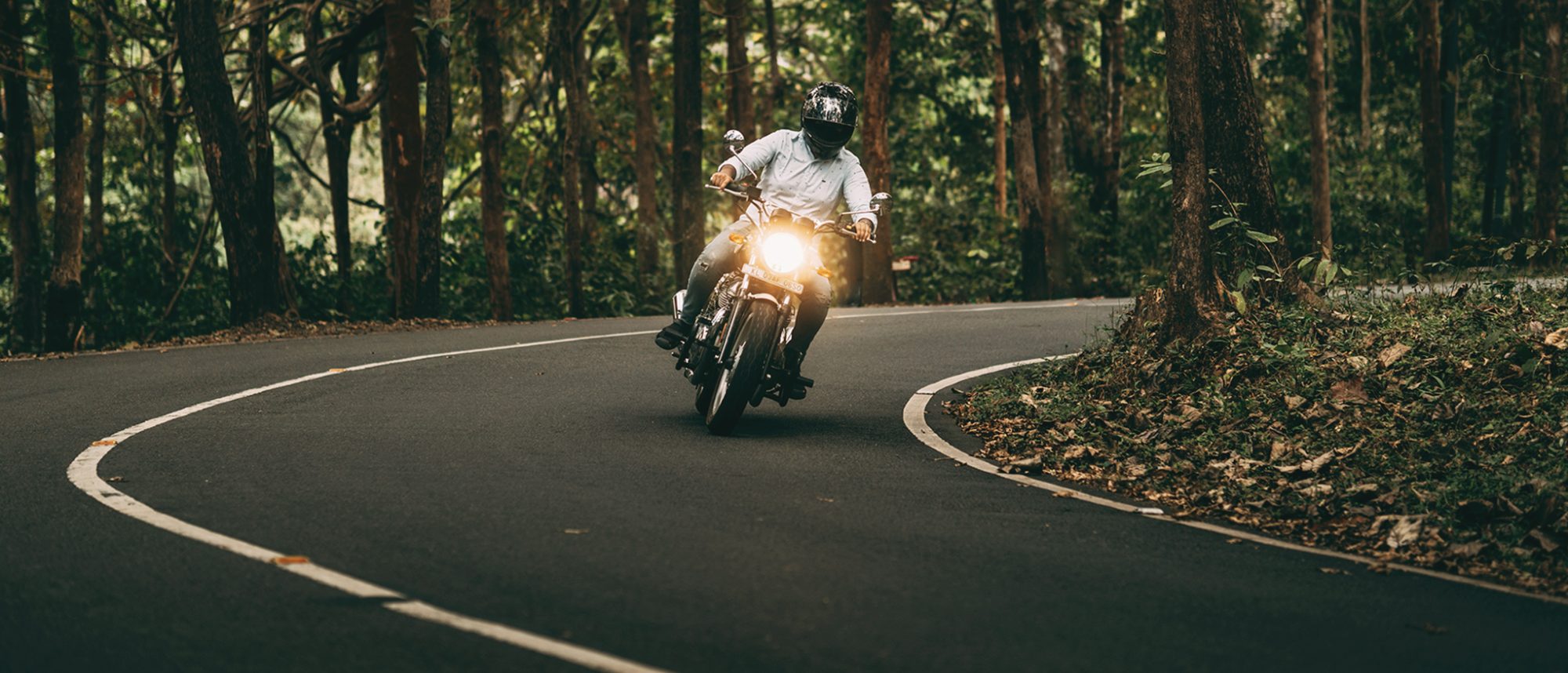 A helmeted rider taking a forest curve with the headlight on